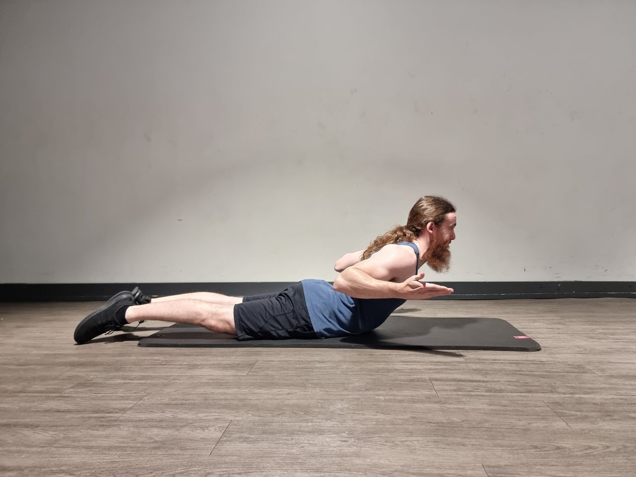 A man performing a swimmers exercise – prone with spinal hyperextension, and elbows pulled back and up